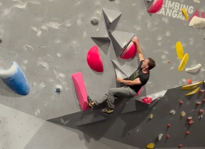 Daniel climbing a route with pink holds in a bouldering gym